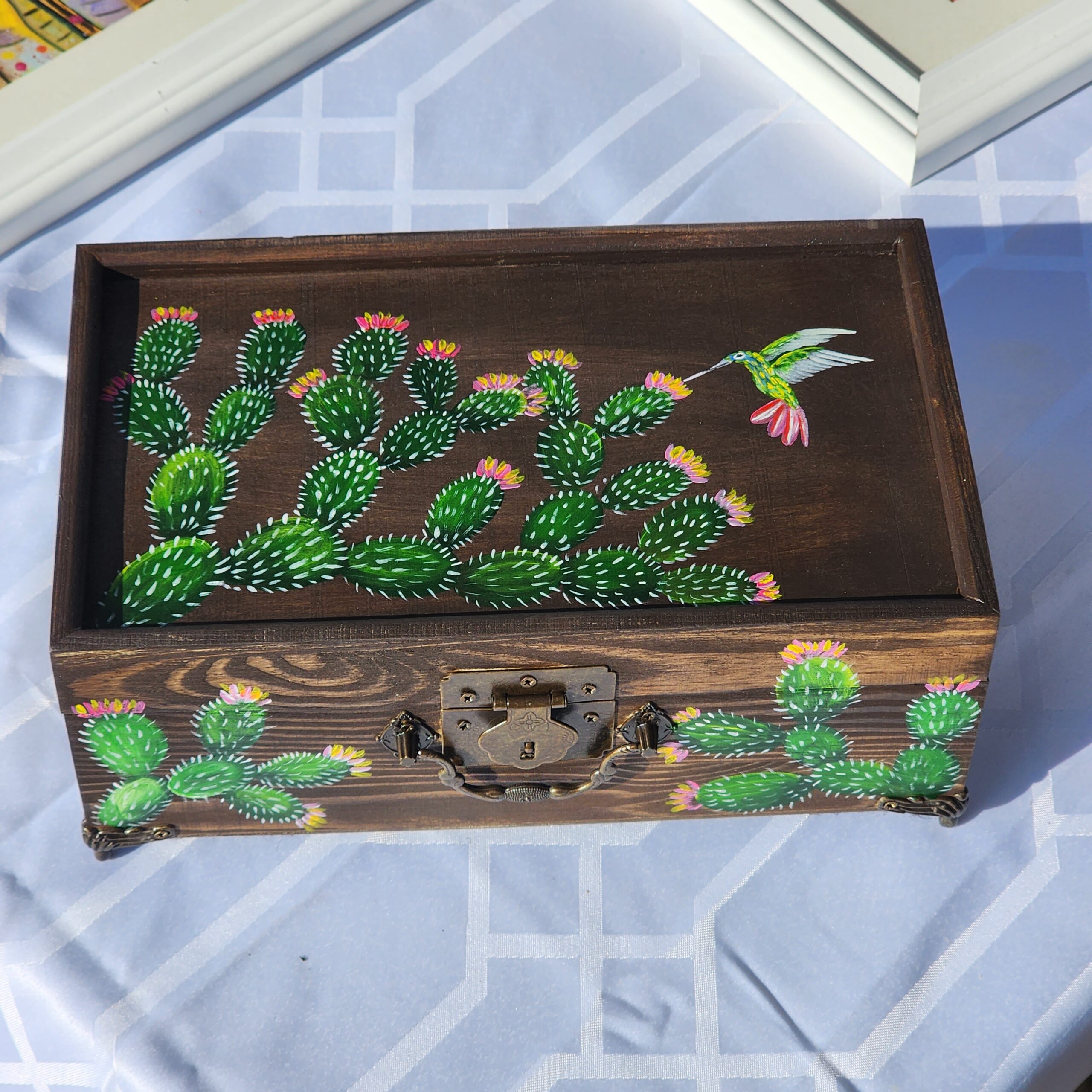 Beautiful handpainted wooden trinket box with a mirror and metal feet. This cute cacti and hummingbird trinket box is an ideal gift for a special loved one. You can store jewelry such as rings, necklaces, bracelets, or anything you would like to keep in a particular place, especially in this elegant and artistic trinket box.