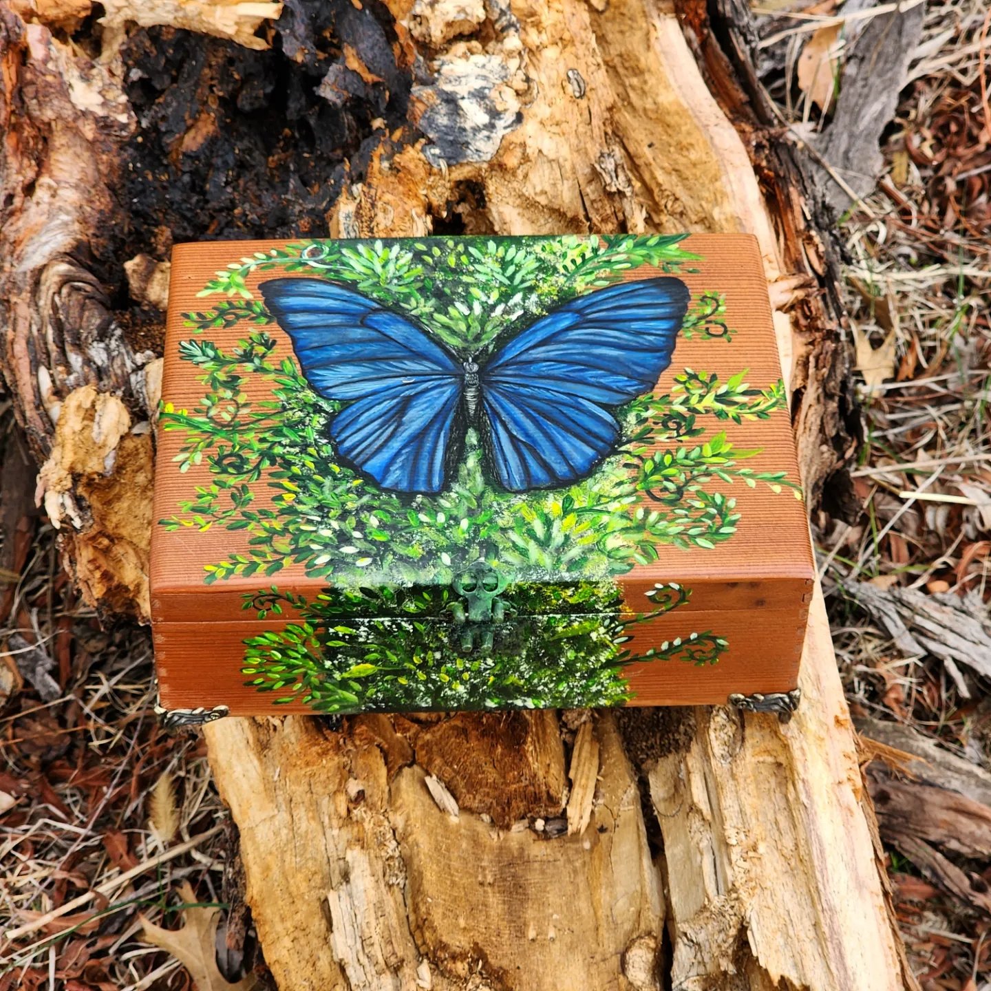 Antique wooden trinket box made of cedar wood. Handpainted with acrylic paint. Metal feet and lock. Made with love and dedication. Blue morpho butterfly sitting on top of a tree full of moss.