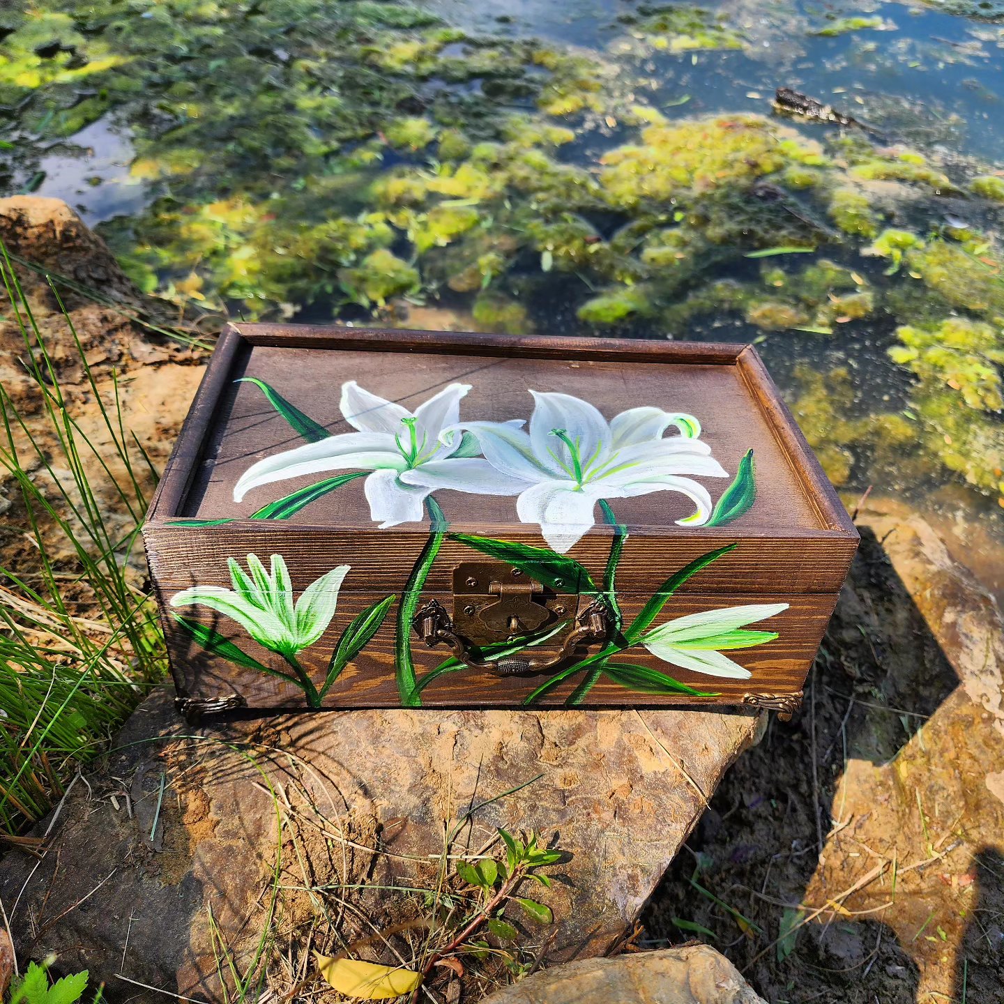 Handpainted wooden jewelry box with original design of white asiatic lilies. This jewelry box comes with a nice mirror inside, metal feet, and bronze plated clasps. The box includes compartments that lift to store more jewelry.