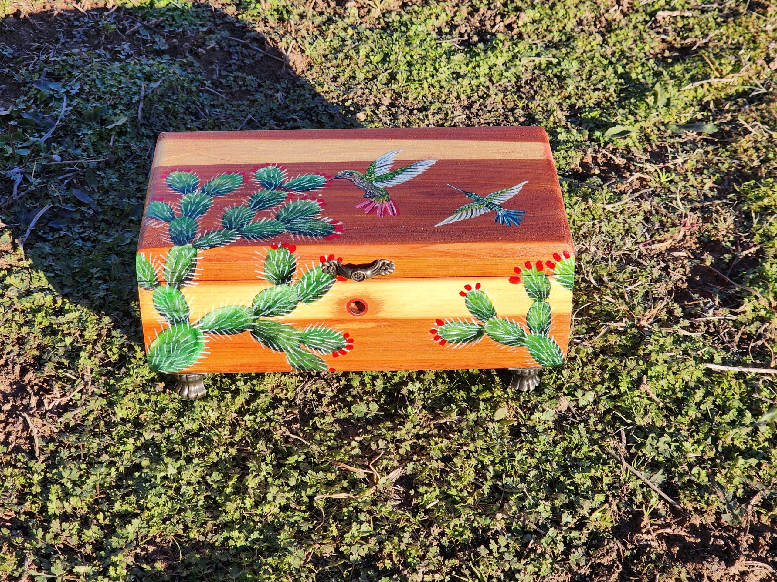 Repurposed antique wooden jewelry box with original design of hummingbirds flying over some cacti. This box used to be a cigar box made of cedar wood. Metal feet and foam ring pad inside.