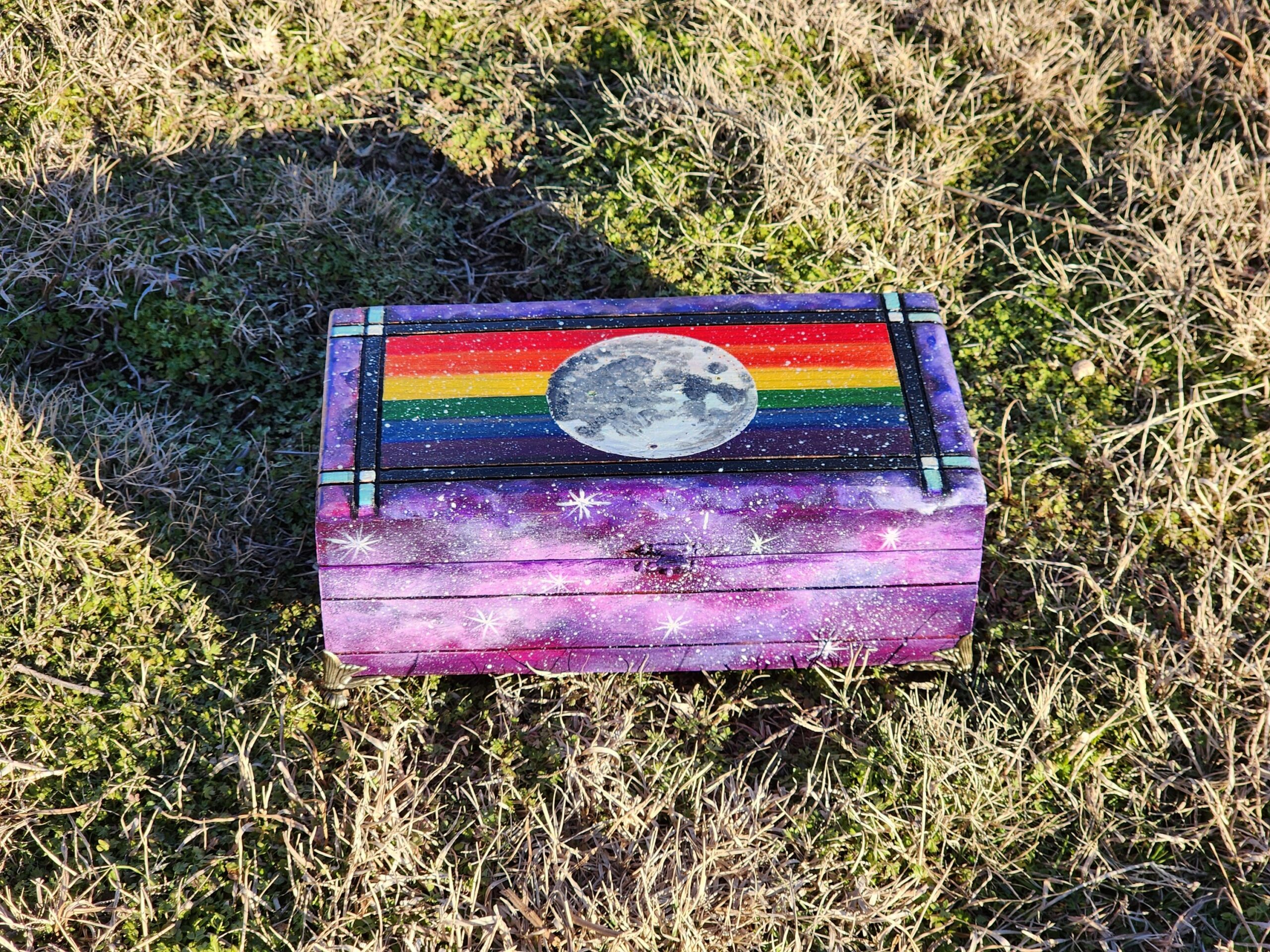 Repurposed antique wooden jewelry box with original design of moon and a galaxy with a rainbow design. Original lock clasp and antique brass feet.