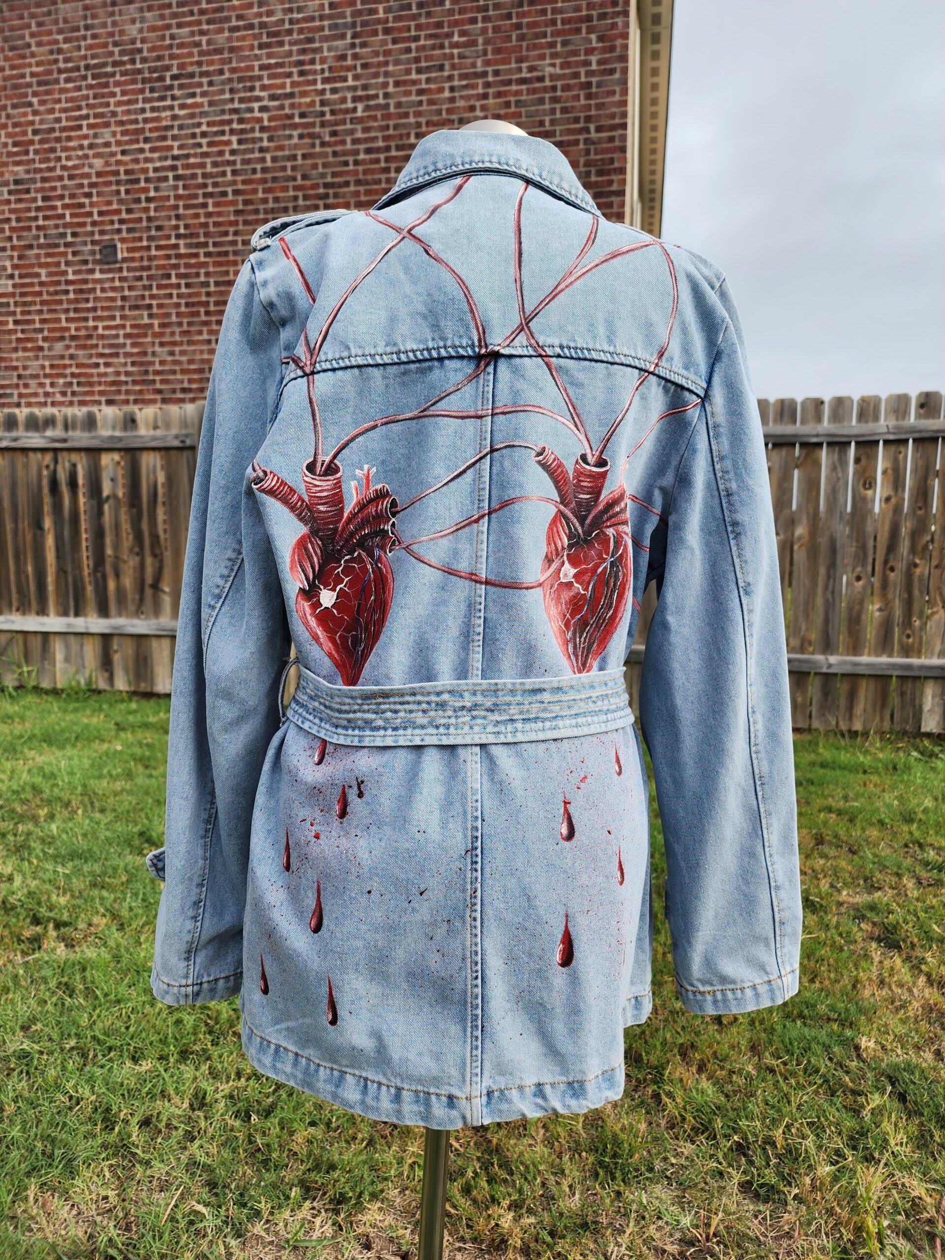 This a women's large handpainted denim trench coat with a magnificent design of two intertwined hearts connected with arteries. Textile paint on denim. Washer and dryer safe.